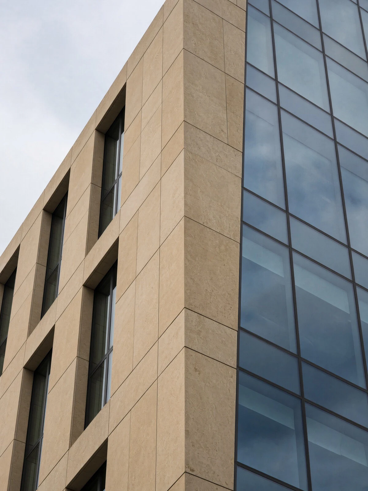 Detail of a stone facade meeting a vertical glass facade.